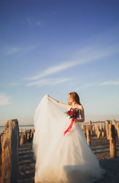 Pretty lady, bride posing in a wedding dress near sea on sunset