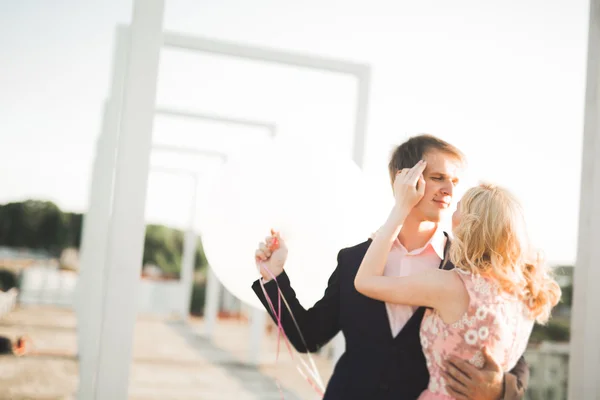 Young couple in love posing on roof with perfect city view holding hands and hugging . Beautiful sunset