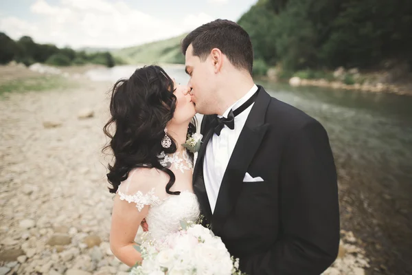 Close up portrait of couple against river and green trees. Beautiful young woman kissing handsome man outdoors