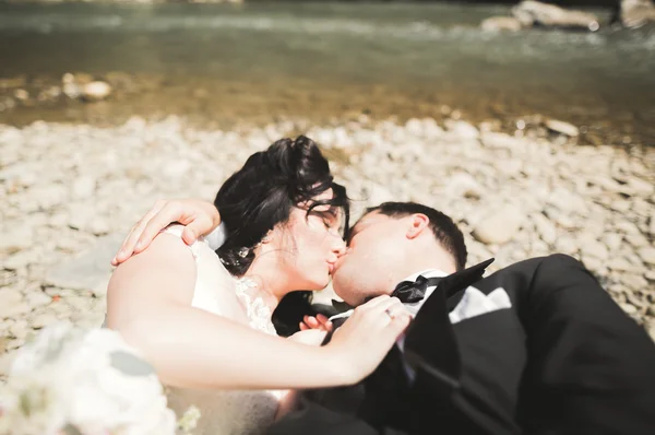 Close up portrait of couple against river and green trees. Beautiful young woman kissing handsome man outdoors