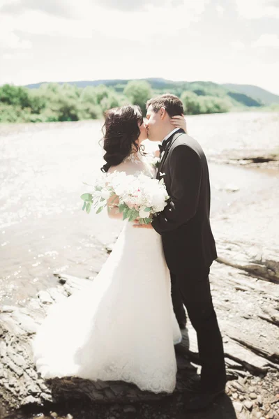 Close up portrait of couple against river and green trees. Beautiful young woman kissing handsome man outdoors