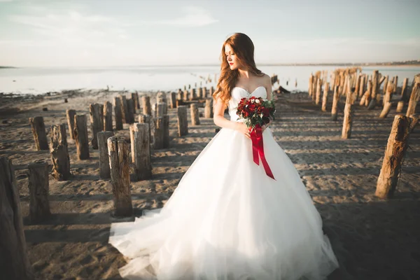 Pretty lady, bride posing in a wedding dress near sea on sunset