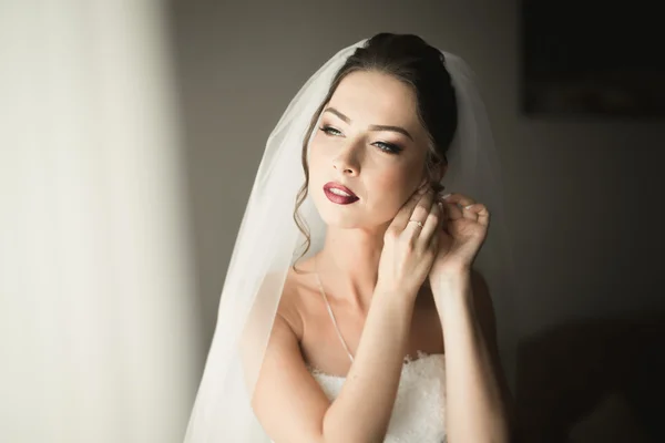 Beautiful young bride with makeup and hairstyle in bedroom, newlywed woman final preparation for wedding. Happy girl waiting groom. Portrait soft focus