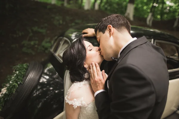 Beautiful newlywed couple posing near retro black car