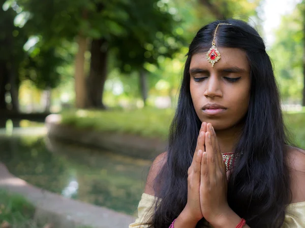 Beautiful young indian woman praying in the park