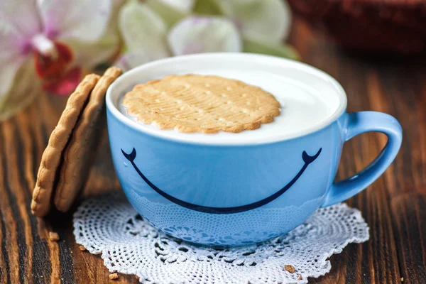 Good morning or Have a nice day message concept - bright blue cup of milk with cookies. Cup of milk with smile. Health and diet concept on the wooden table, close up.
