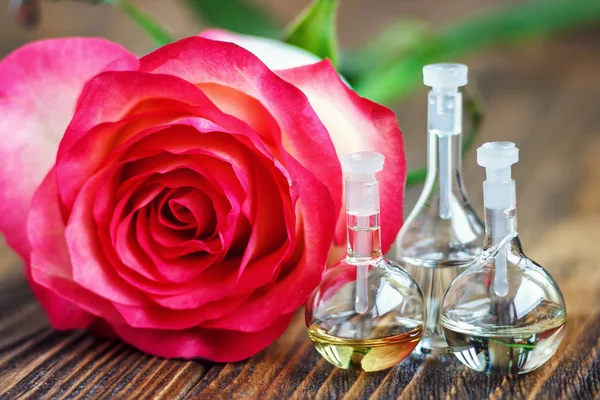 Essential oil in glass bottle with rose flowers on wooden background. Small bottles of perfume. Beauty treatment. Spa concept. Selective focus.