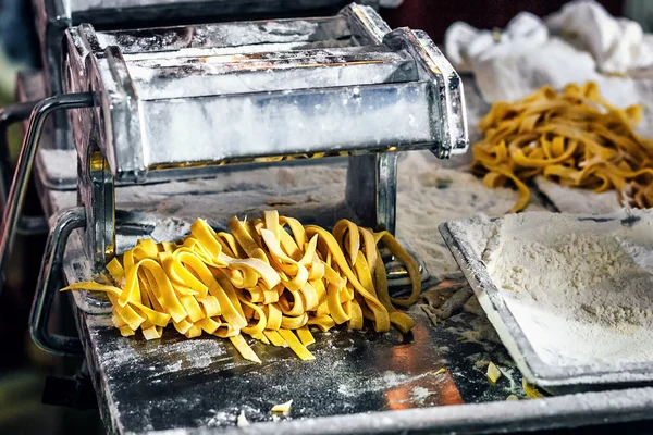 Fresh pasta and pasta machine on kitchen table. Fettuccine homemade. Process of making homemade pasta linguine, closeup.