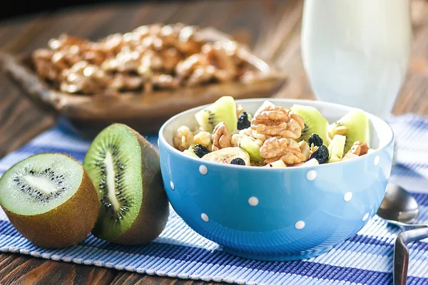 Organic oatmeal porridge in ceramic bowl with bananas, honey, walnuts, kiwi fruit and raisins. Healthy breakfast - health and diet concept on the wooden table, close up