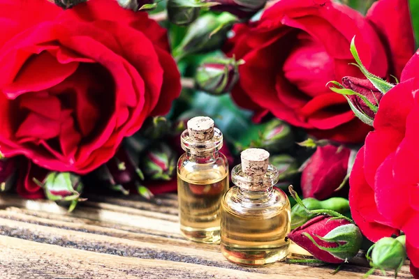 Essential oil in glass bottle with red rose flowers and petals on wooden background. Beauty treatment. Spa and aromatherapy concept. Selective focus.