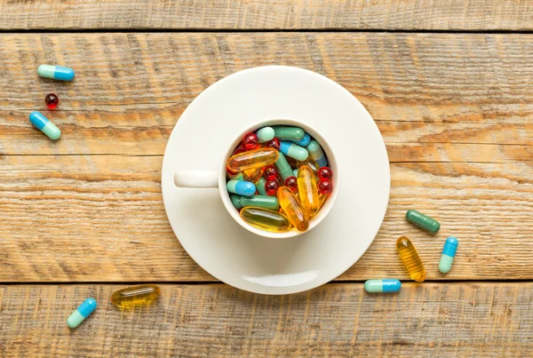 Many colorful pills in cup on wodden table