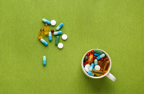 Colorful medical pills in cup on green background