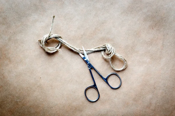 Scissors cut the knot on rope at background kraft paper