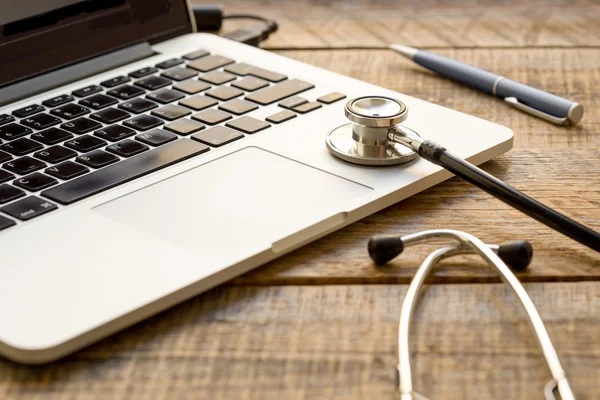 Doctor workplace with a stethoscope and laptop at wooden table