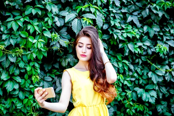 Young woman in bushes summer in yellow dress making selfie