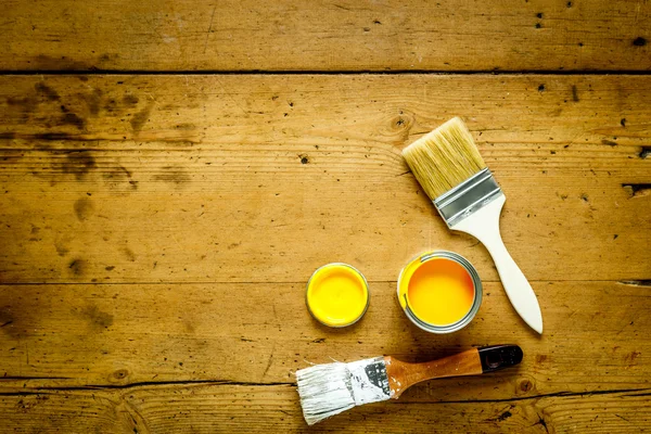Can with yellow paint and brush on wooden background