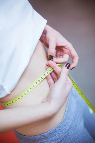 Healthy lifestyle. slender young girl in a white shirt and gray sweat pantswith measuring tape in hand measures the waist