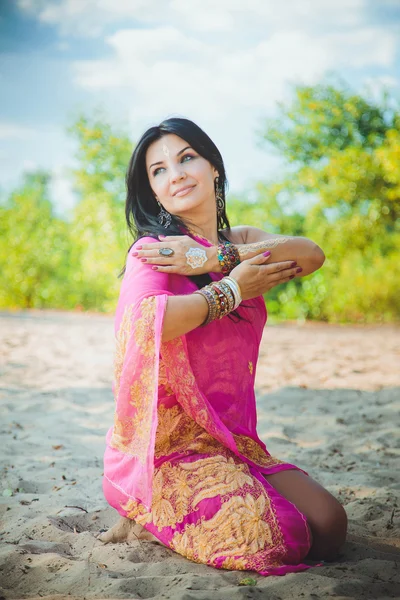 Beautiful caucasian brunette woman in dress in oriental style with oriental patterns on her hands and face, with bracelets in oriental style. Indian woman