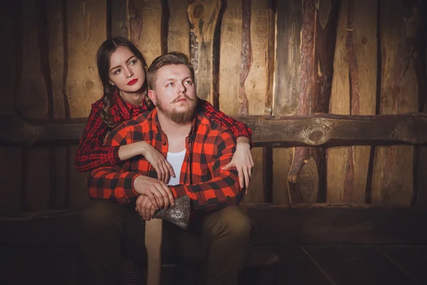 Style lumberjack. Woodcutter with a beard and mustache, wearing a red shirt, pants and suspenders and his girlfriend on a wooden background. Modern style.Loving couple of caucasian in style Lumberjack