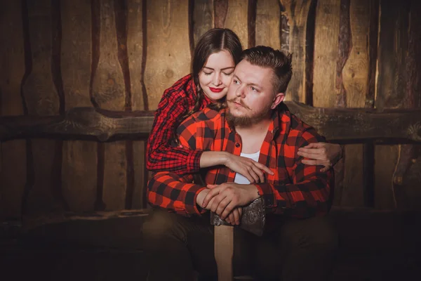 Style lumberjack. Woodcutter with a beard and mustache, wearing a red shirt, pants and suspenders and his girlfriend on a wooden background. Modern style.Loving couple of caucasian in style Lumberjack