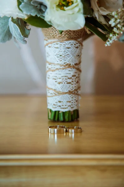 Two gold wedding rings  lying  on a light wooden table next to  a bridal bouquet Rustic