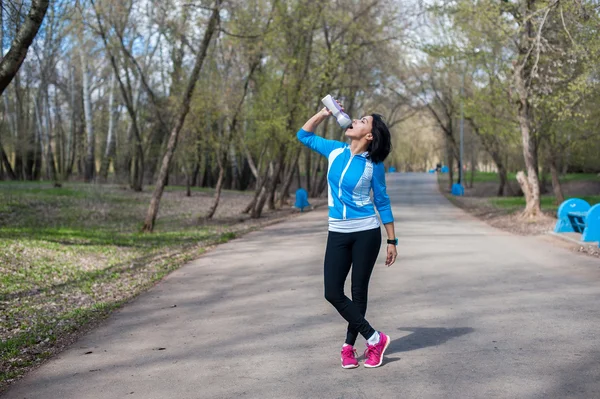 Athletic woman standing in a Park and drinking water