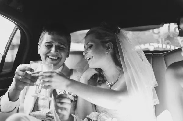 The bride and groom in car smiling happily and drinking champagne