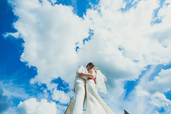 The bride and groom with wings of clouds are in the sky and kiss