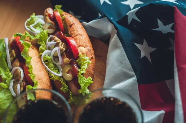 Two fresh hot dogs on a wooden Board, glasses with Cola and American flag