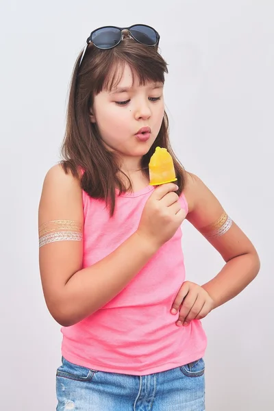 Girl eating ice cream in a pink t-shirt and torn fashionable jeans with temporary tattoos on their hands on a light background