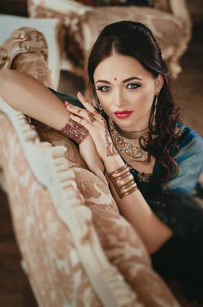 Portrait of a beautiful woman in Indian traditional Chinese dress, with her hands painted with henna mehendi. Girl sitting on a luxury sofa