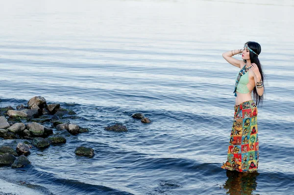 Beautiful slim woman with long black hair and a bandage on his head, in the clothes in boho style, standing in water. Boho chic style