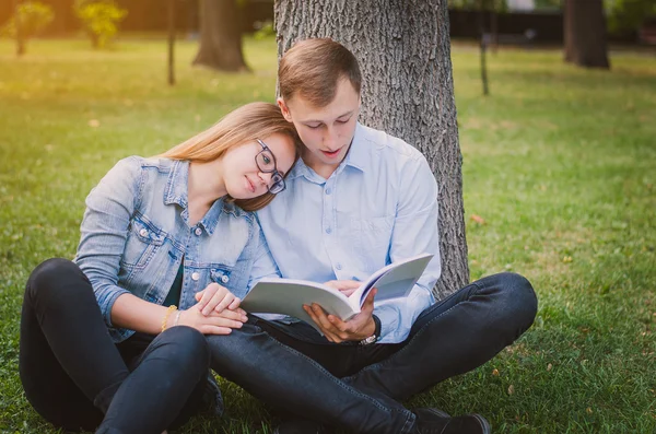 Students guy and the girl in the park sitting on the grass and reading a book. Education concept