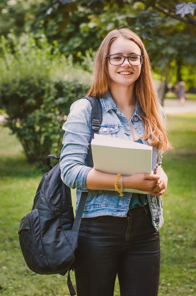 Happy cute young smiling girl student in the park with books and backpack