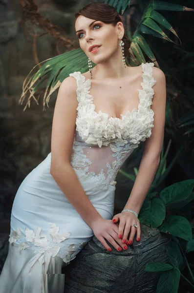 Beautiful young brunette woman in a long white dress, blue eyes, in the jungle. Bride in the jungle.