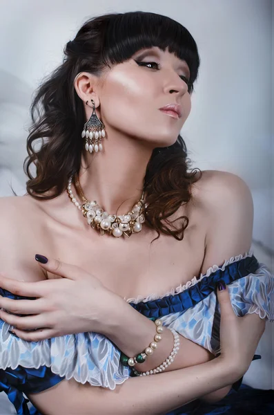 Portrait of a beautiful brunette in a blue dress with a vintage historic bared shoulders in necklace and earrings with eyes closed