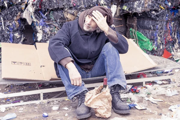 Homeless man with a bottle of red wine in landfill