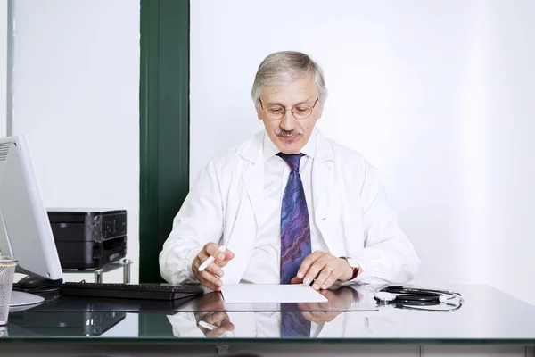 Mature male doctor sitting at desk in doctor\'s room