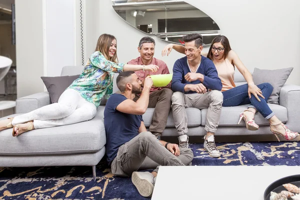 Group of friends watching tv and eating popcorn on sofa