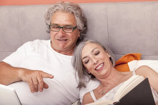 Mature couple relaxing in bed reading a book