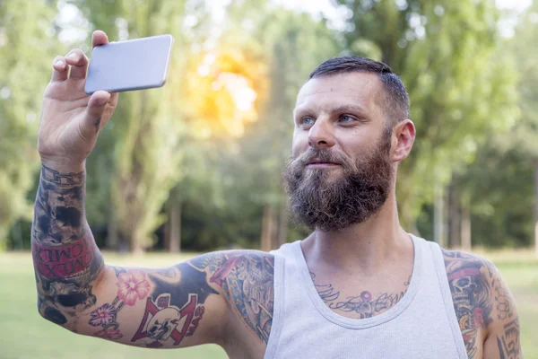 Tattooed bearded man takes a selfie in the park