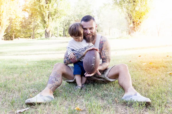 Tattooed father have fun with his son in the park with rugby bal