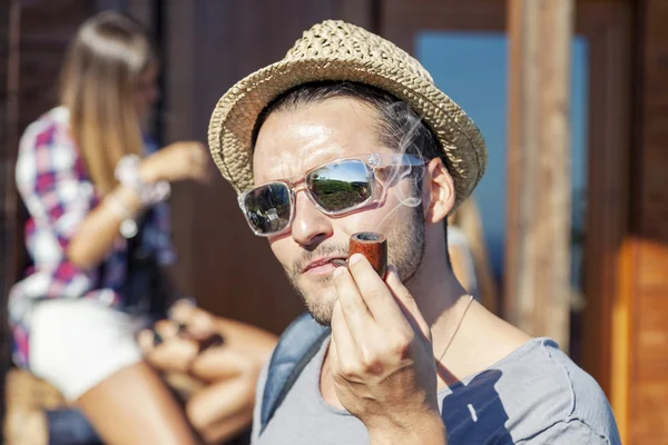 Young hiker lights his pipe in front of the hut