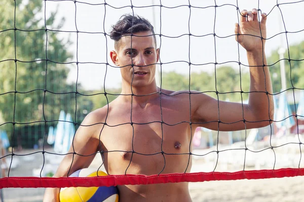 Portrait of volleyball player standing in front of net at beach