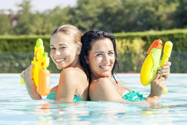 Pretty girls playing with water guns in pool