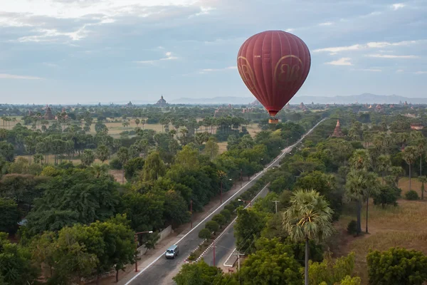 Old Bagan, Burma. December 1, 2011: Hot air balloons fly in the sky over a road in the savanna