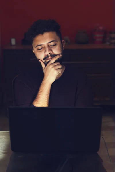 Young man looking at laptop and thinking in dark room