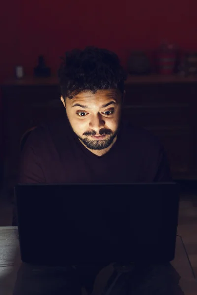 Amazed young man looking at laptop computer in dark