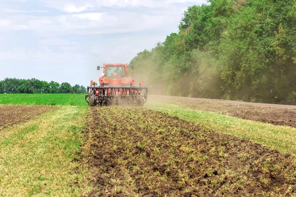 Modern tech red tractor plowing a green agricultural field in spring on the farm. Harvester sowing wheat.