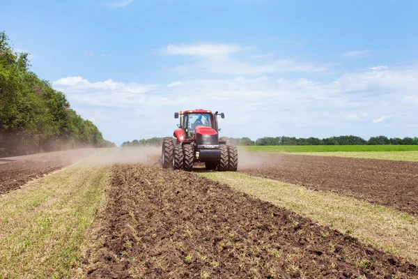 Modern tech red tractor plowing a green agricultural field in spring on the farm. Harvester sowing wheat.